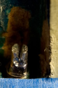 Tengelyirányú vágat, hogy csavarhúzóval forgassam. Középen a beletört acéltüske, ami egy percenként nyírta le a fűrészfogakat.